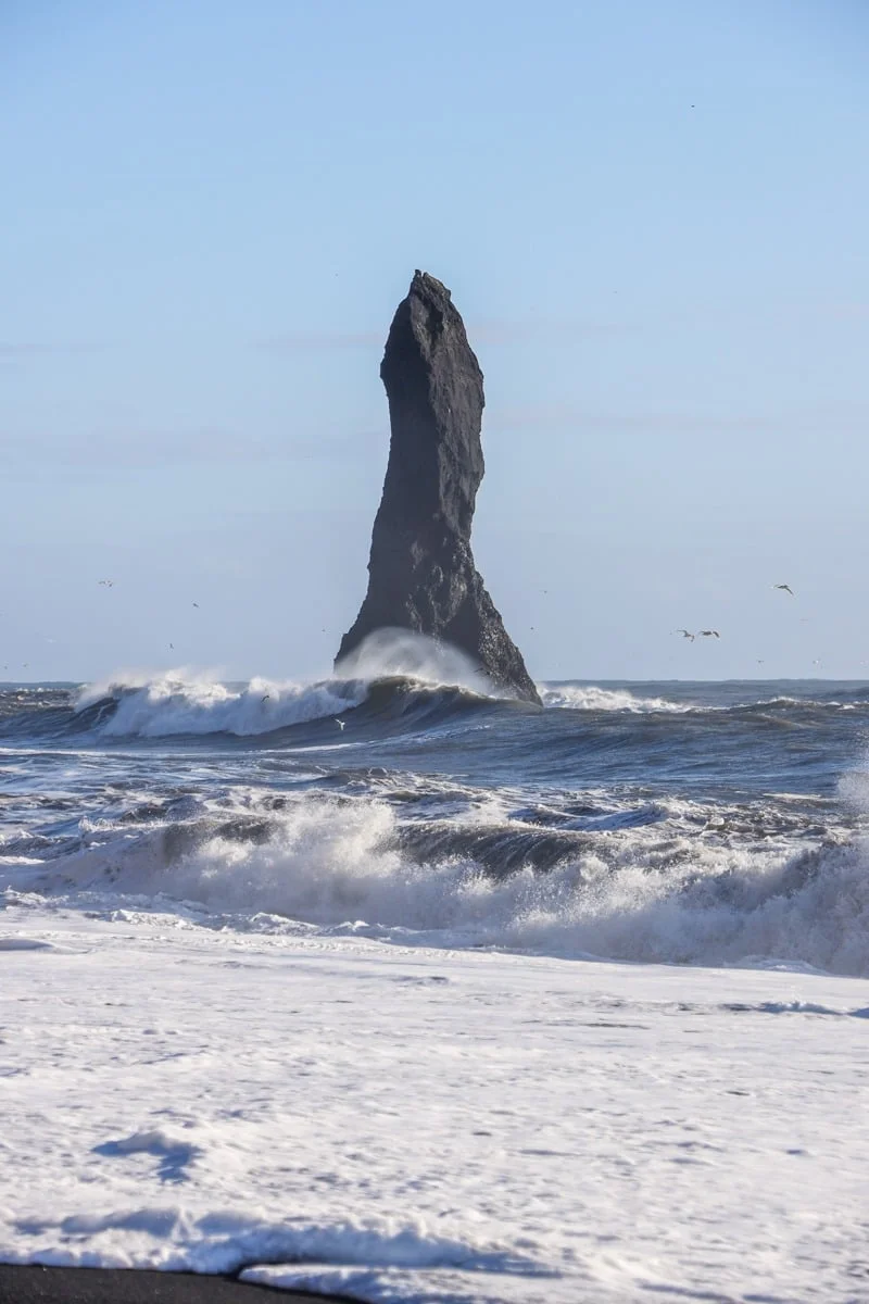 Rocher basaltique élancé entouré de vagues et d'oiseaux