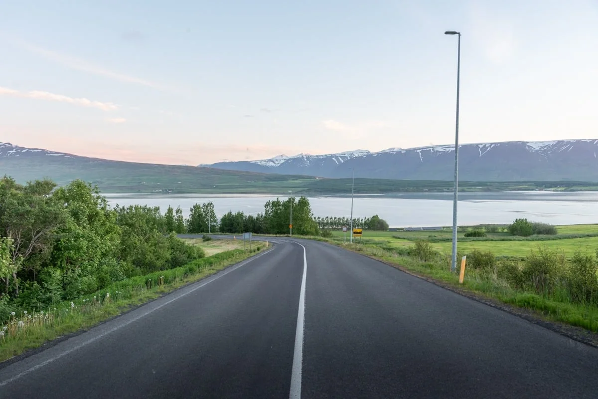 Route asphaltée sinueuse longeant un fjord avec montagnes enneigées en fond