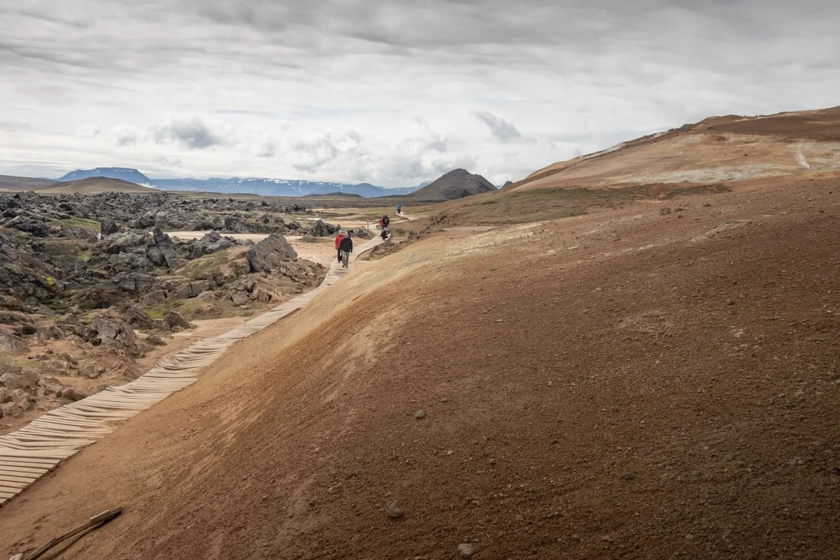 Randonneurs sur un sentier en bois traversant un terrain volcanique ocre