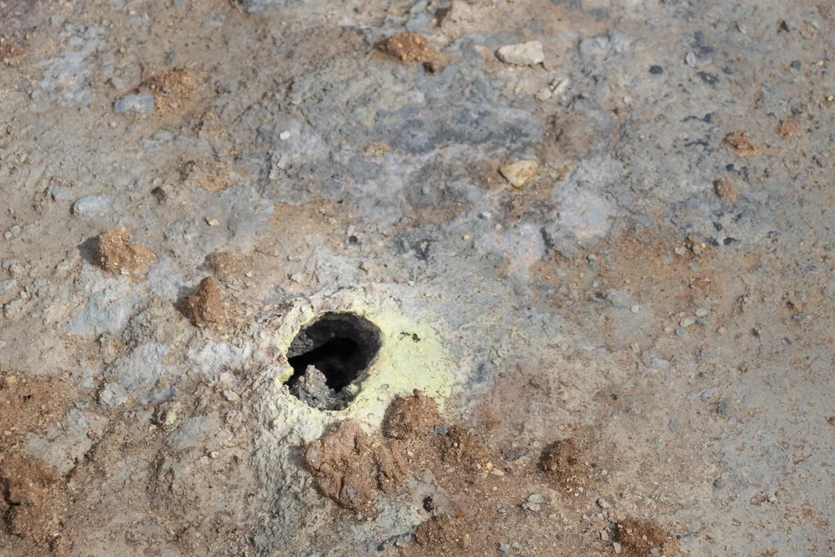 Petit orifice volcanique entouré de dépôts de soufre jaune sur sol aride