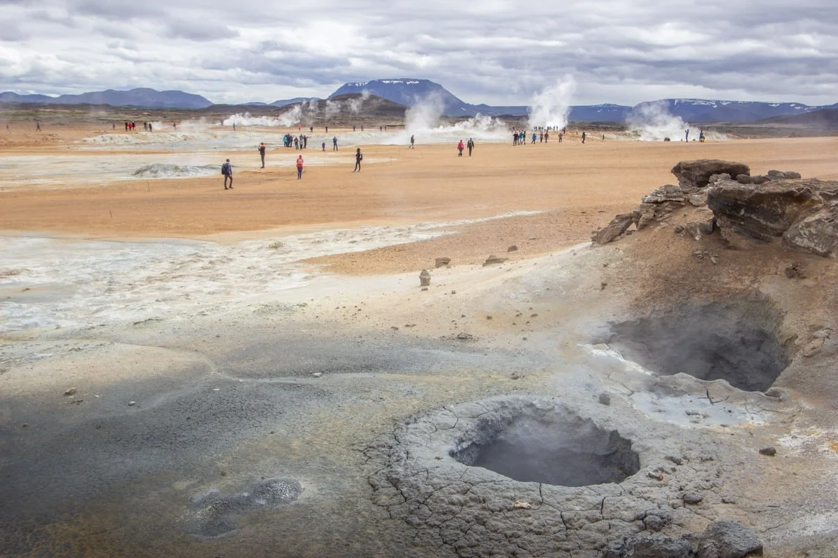 Zone géothermique avec fumerolles, sol ocre et visiteurs dispersés