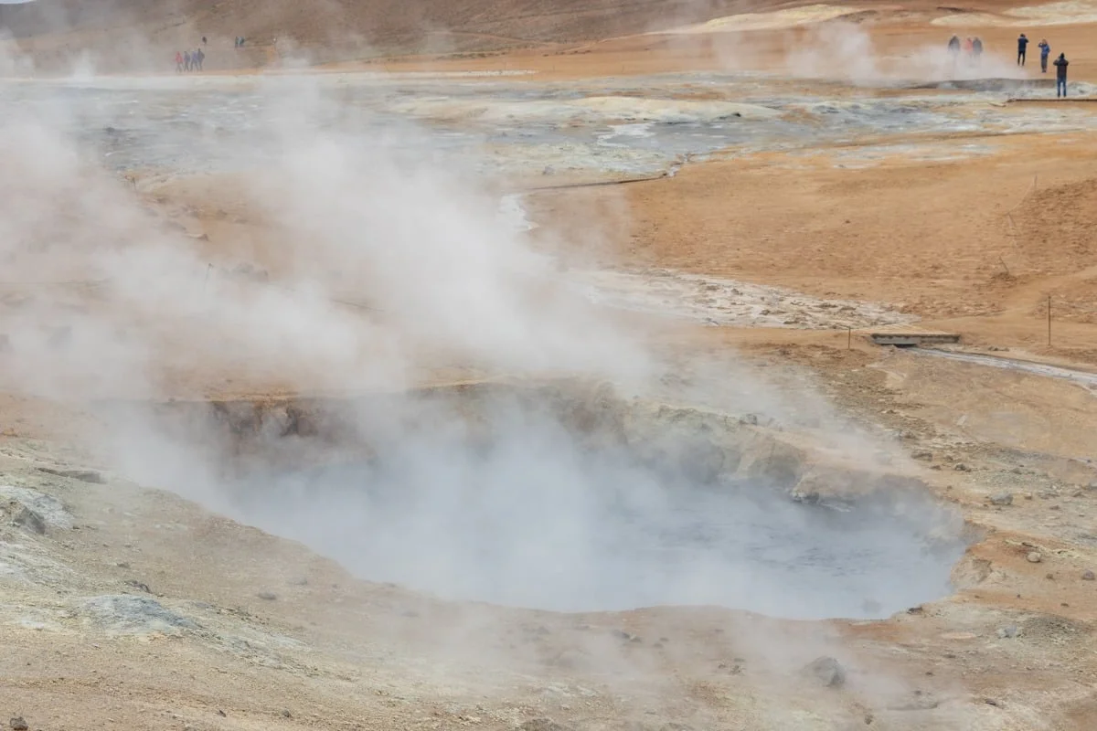 Mare de boue fumante dans un paysage volcanique ocre avec visiteurs