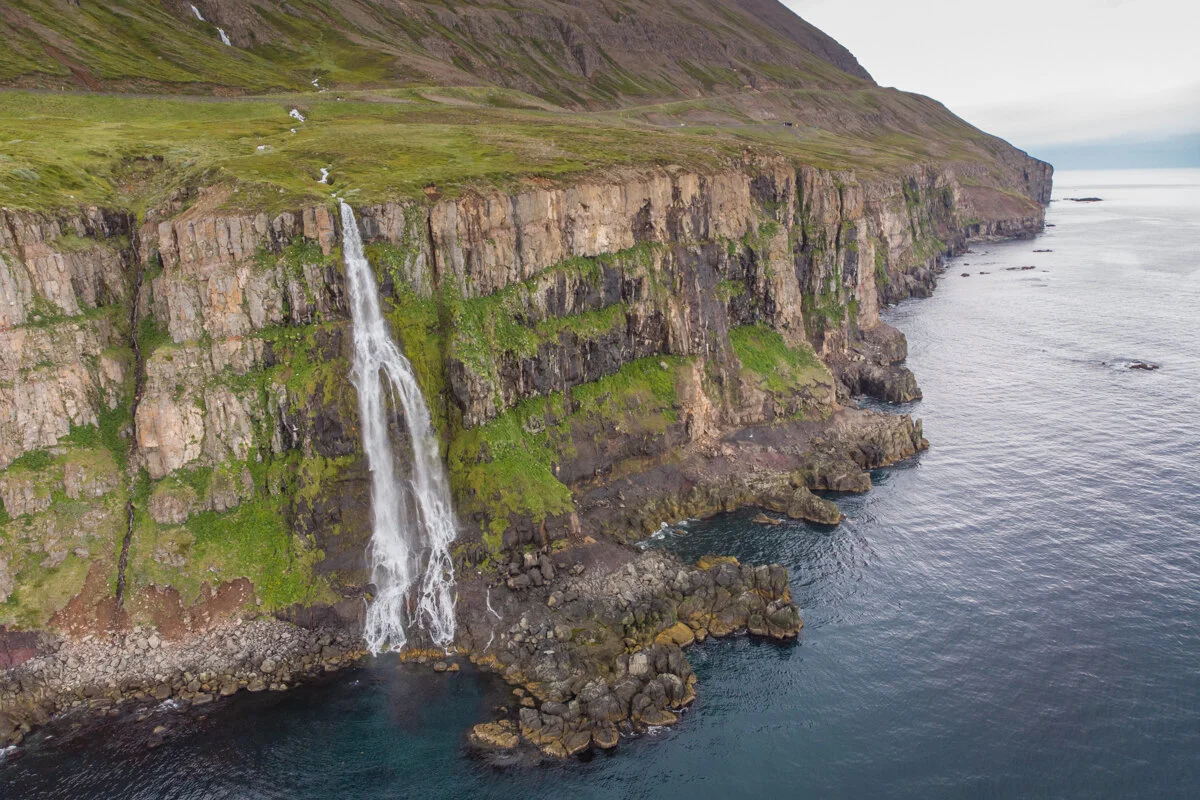une cascade coule d'une falaise côtière vers le fjord, vue depuis les airs