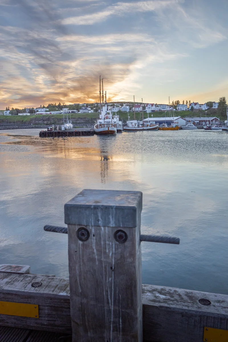 bollard en bois au premier plan avec bateaux et port en arrière-plan, au coucher du soleil
