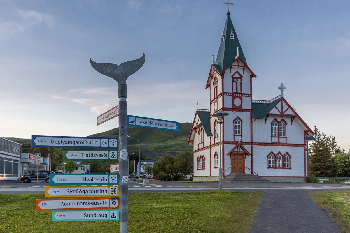 église avec clocher pointu, sculpture de baleine et panneau indicatif