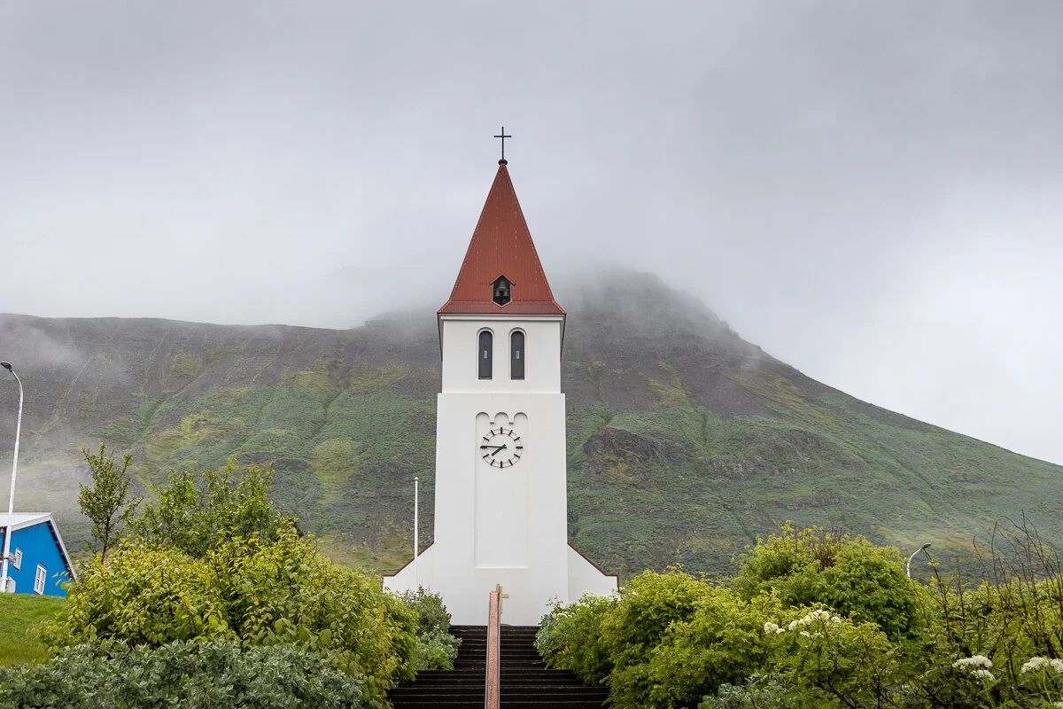 église avec clocher blanc et toit rouge devant une montagne dans la brume