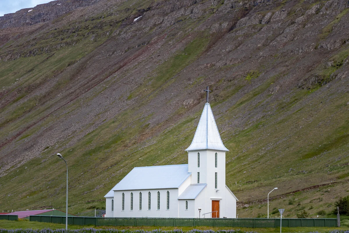 église blanche avec clocher pointu au pied d'une montagne