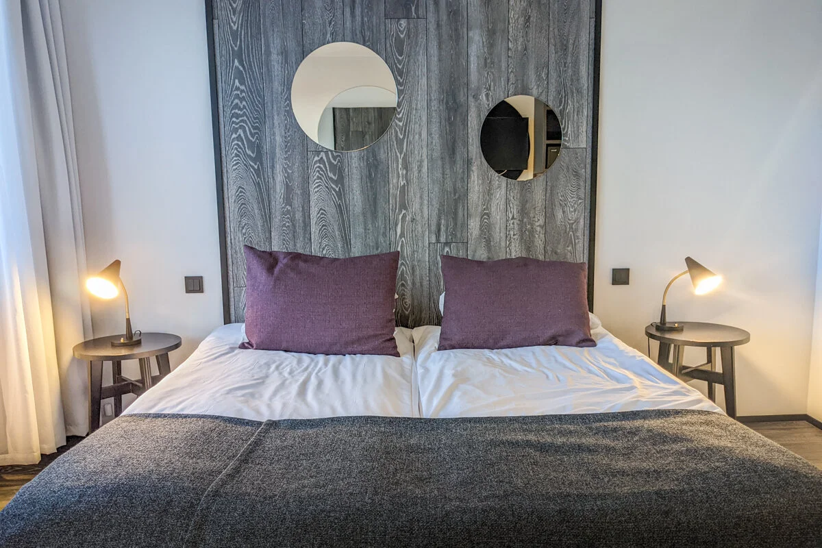 chambre avec lit double aux coussins violets et tête de lit grise