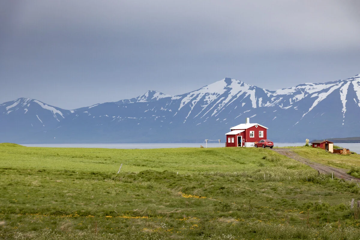 maison rouge isolée dans une prairie avec montagnes enneigées