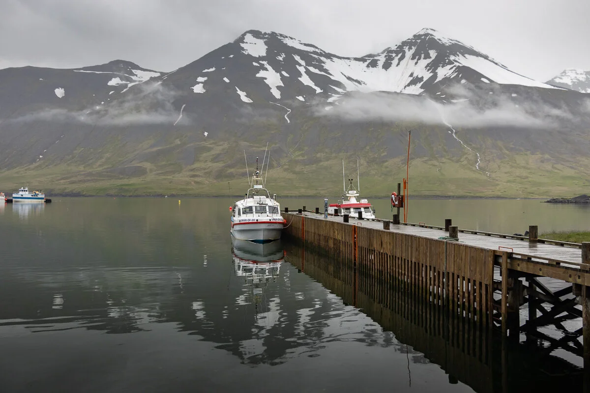 un bateau amarré à un ponton en bois face à des montagnes enneigées