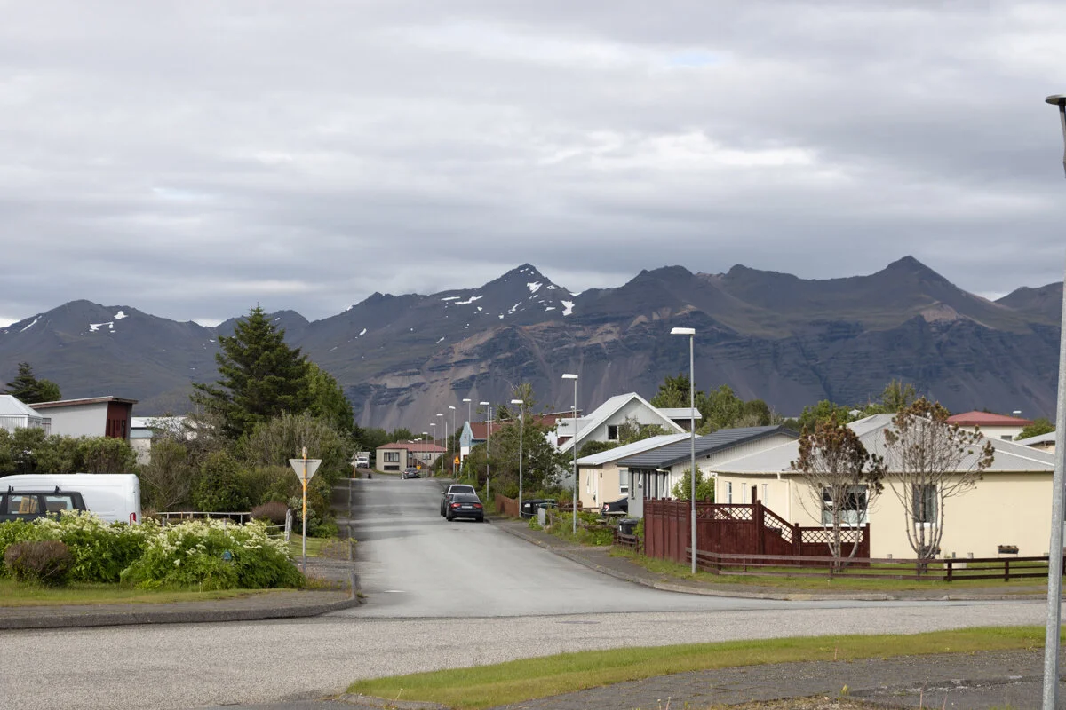 une route devant des maisons avec des montagnes en arrière-plan