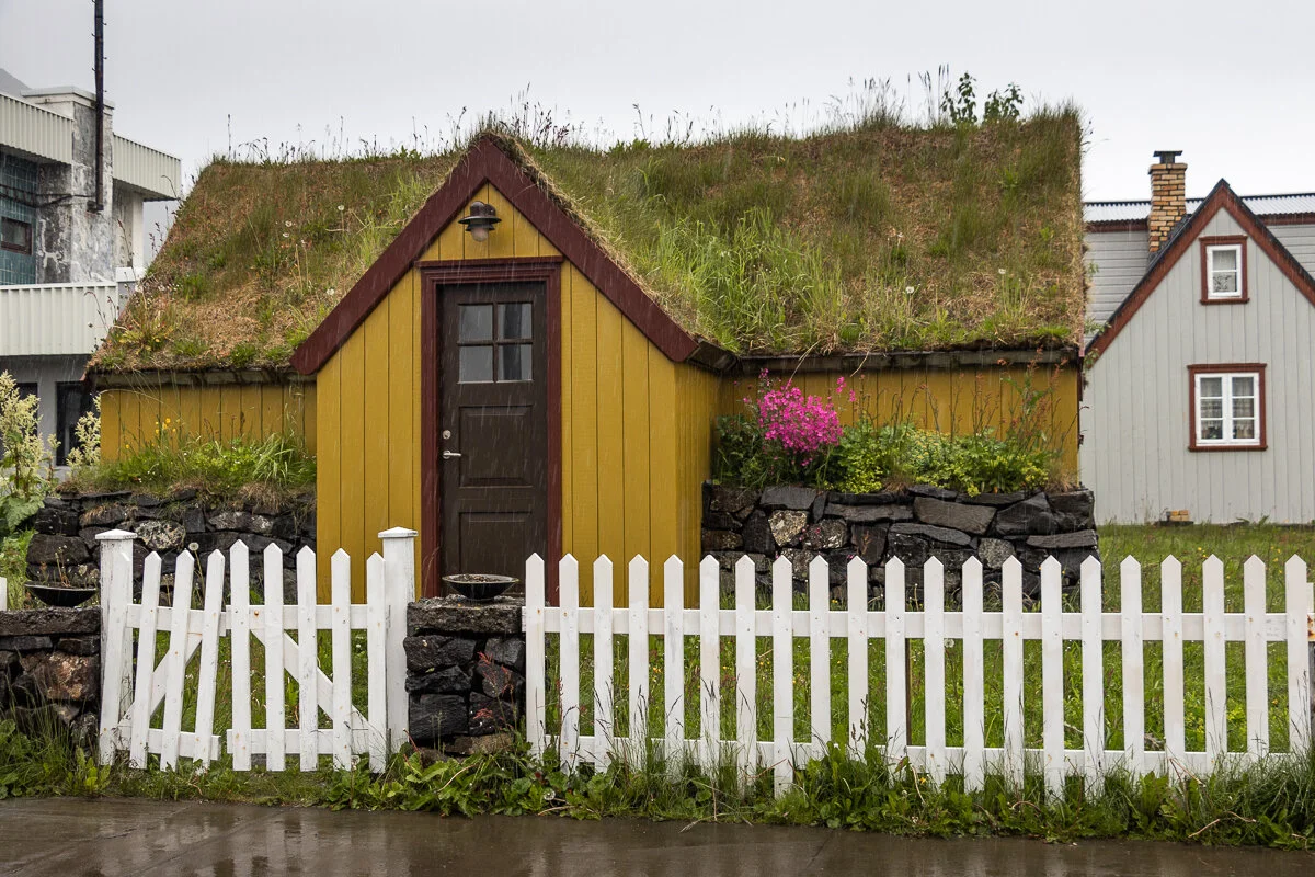 petite maison jaune avec toit en tourbe et clôture blanche