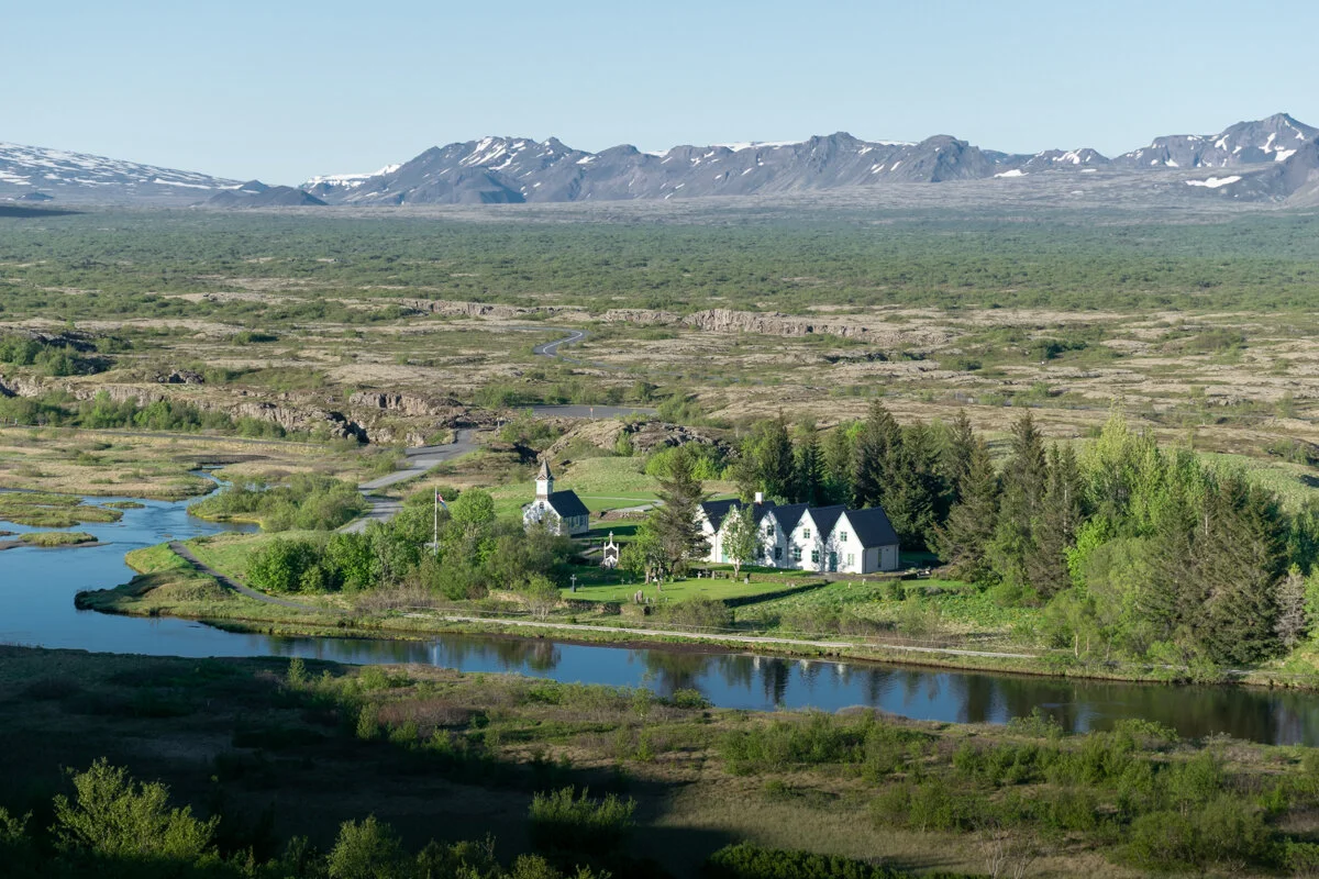 panorama sur Thingvellir avec une maison blanche au bord d'une rivière, entourée de forêt et de montagnes