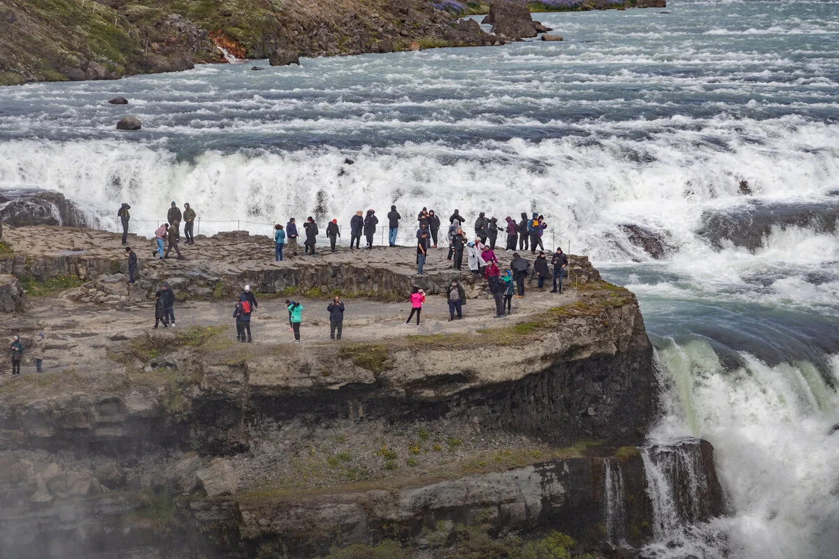 des touristes debout sur un rocher face à la chute d'eau