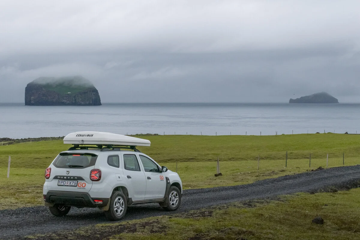 voiture blanche avec une tente de toit garée dans un paysage côtier des avec îles en arrière-plan