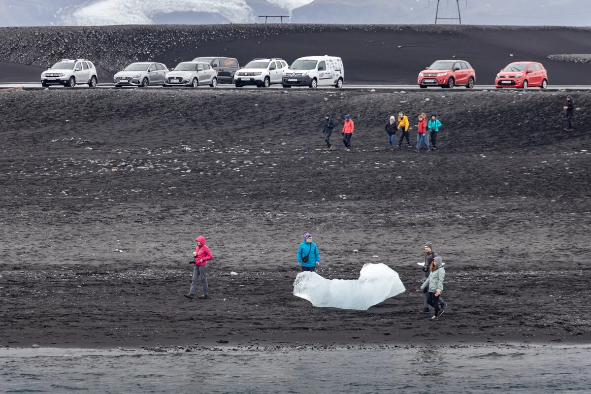 des touristes sur la Diamand Beach avec des voitures garées sur le parking en arrière plan