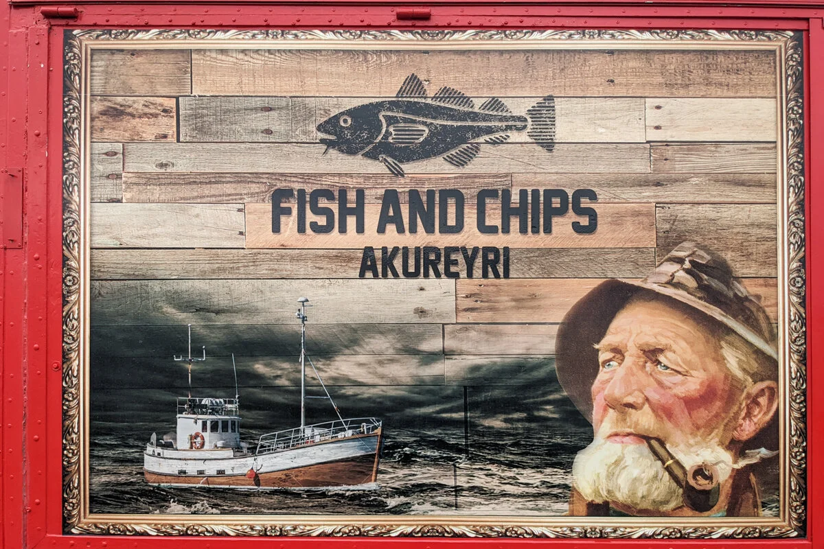 enseigne de restaurant "fish and chips Akureyri" avec dessin d'un pêcheur et d'un bateau