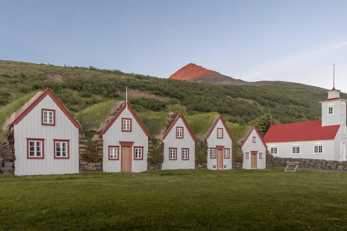 maisons rouges et blanches alignées dans un paysage herbeux, avec de l'herbe sur le toit