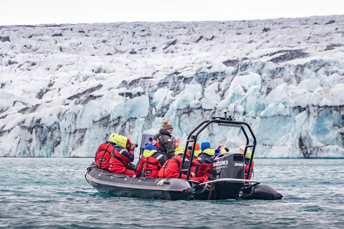 un zodiac avec des passagers en gilets de sauvetage rouges près d'un glacier
