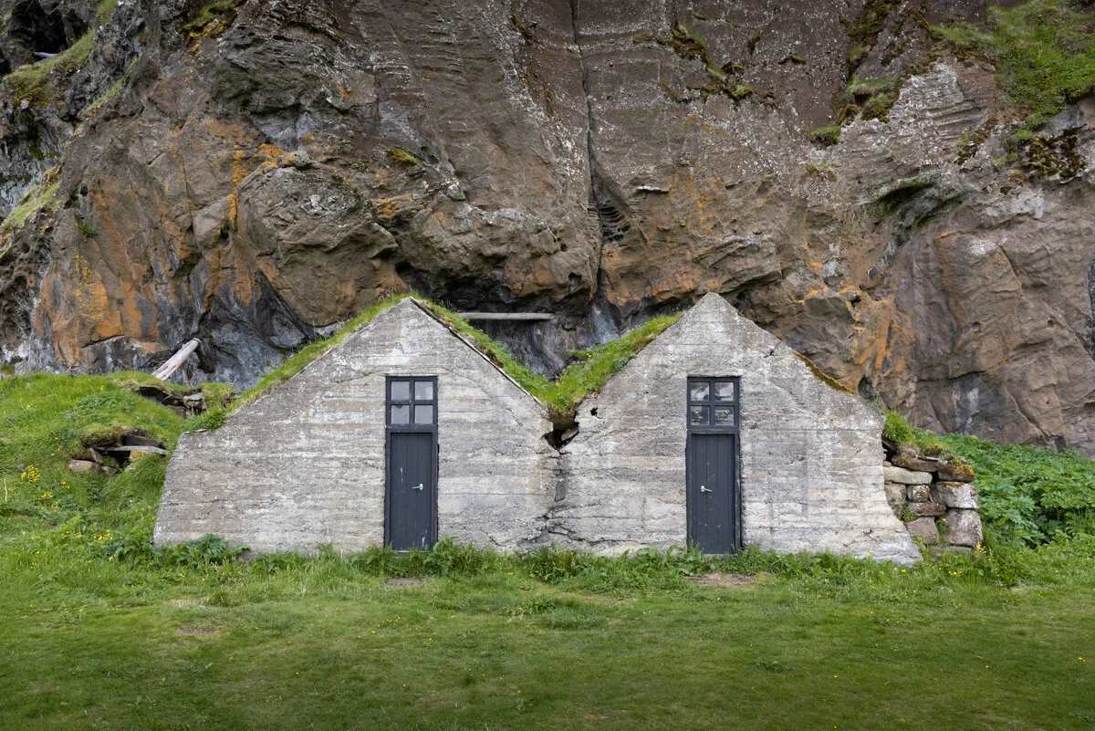 deux petites maisons blanches construites sous une falaise rocheuse avec de l'herbe sur le toit