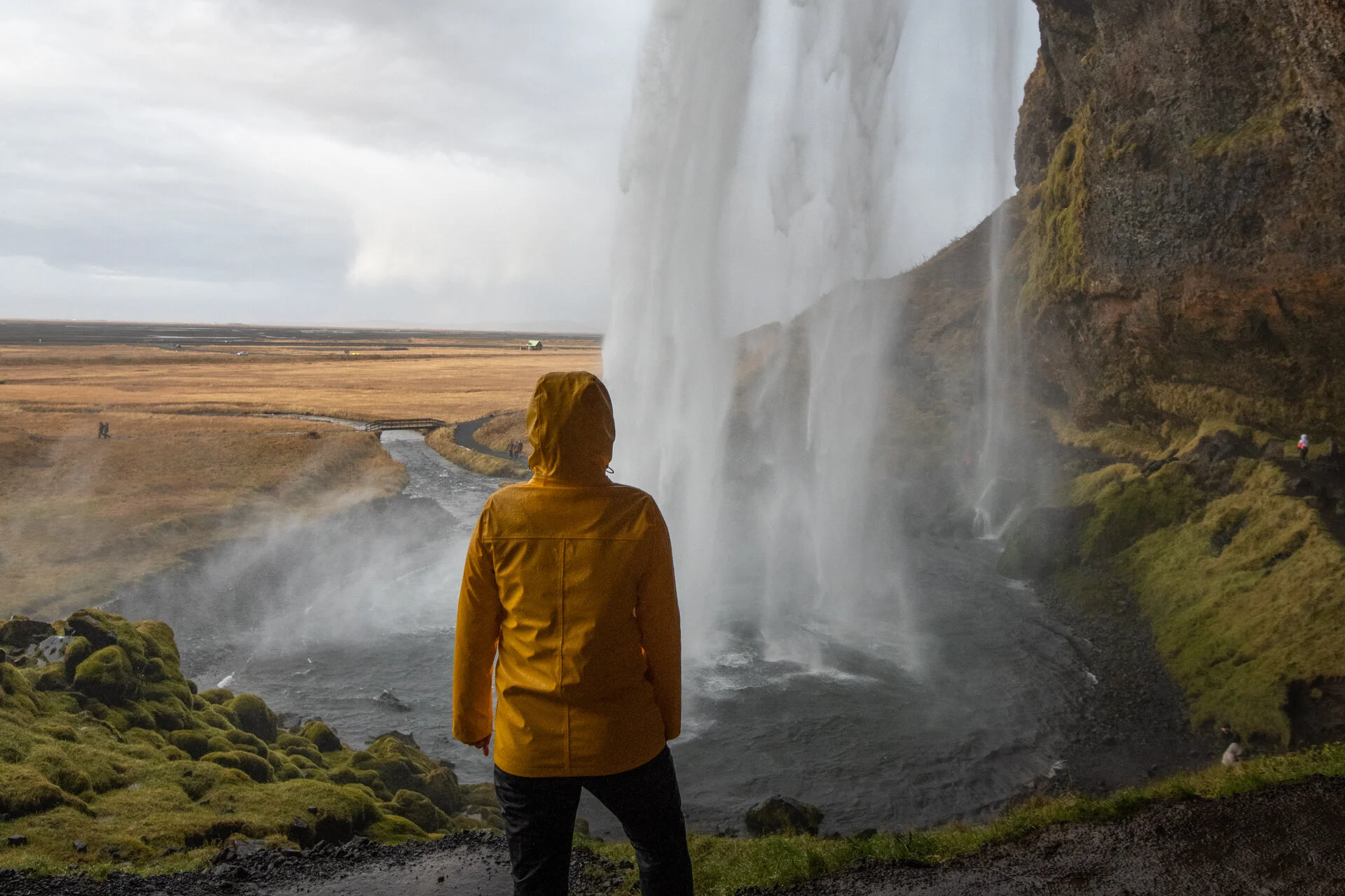 une personne en veste jaune derrière la cascade de Seljalandsfoss