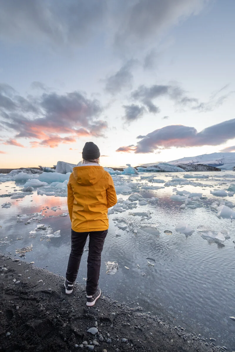 personne en veste jaune face aux icebergs au coucher du soleil