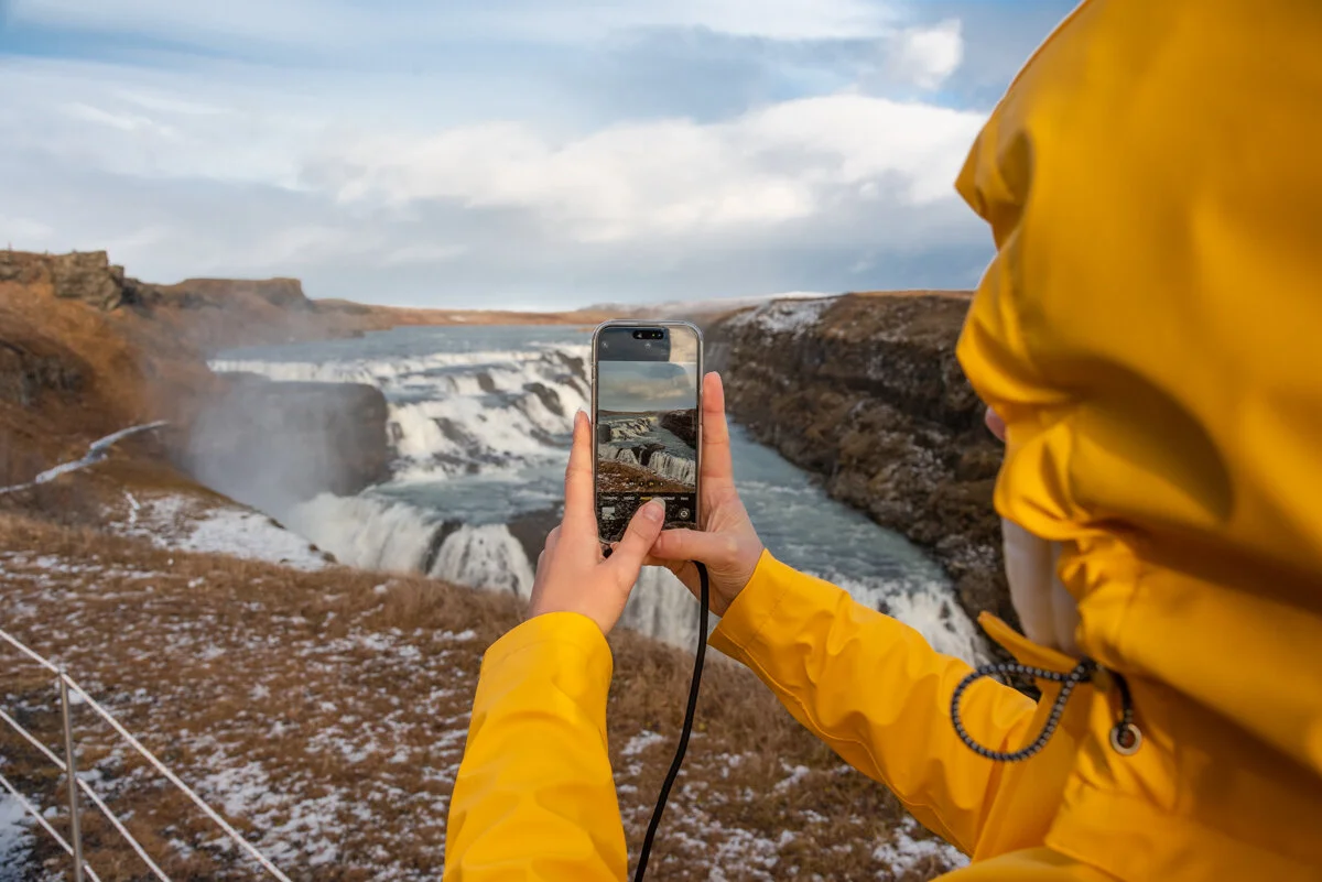 personne en veste jaune photographie une cascade avec un téléphone