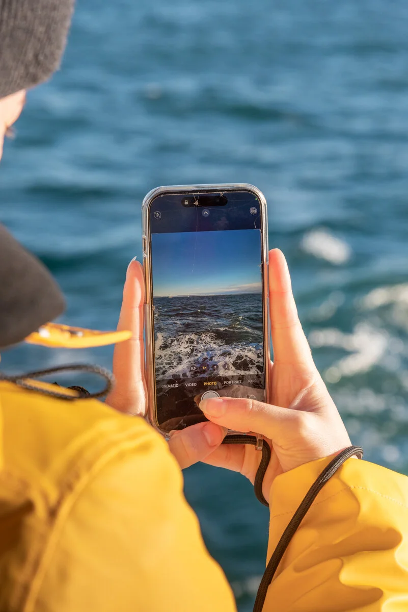 une personne en ciré jaune qui photographie la mer avec un smartphone
