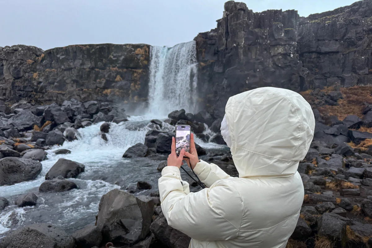 une personne en veste blanche avec capuche qui photographie une cascade