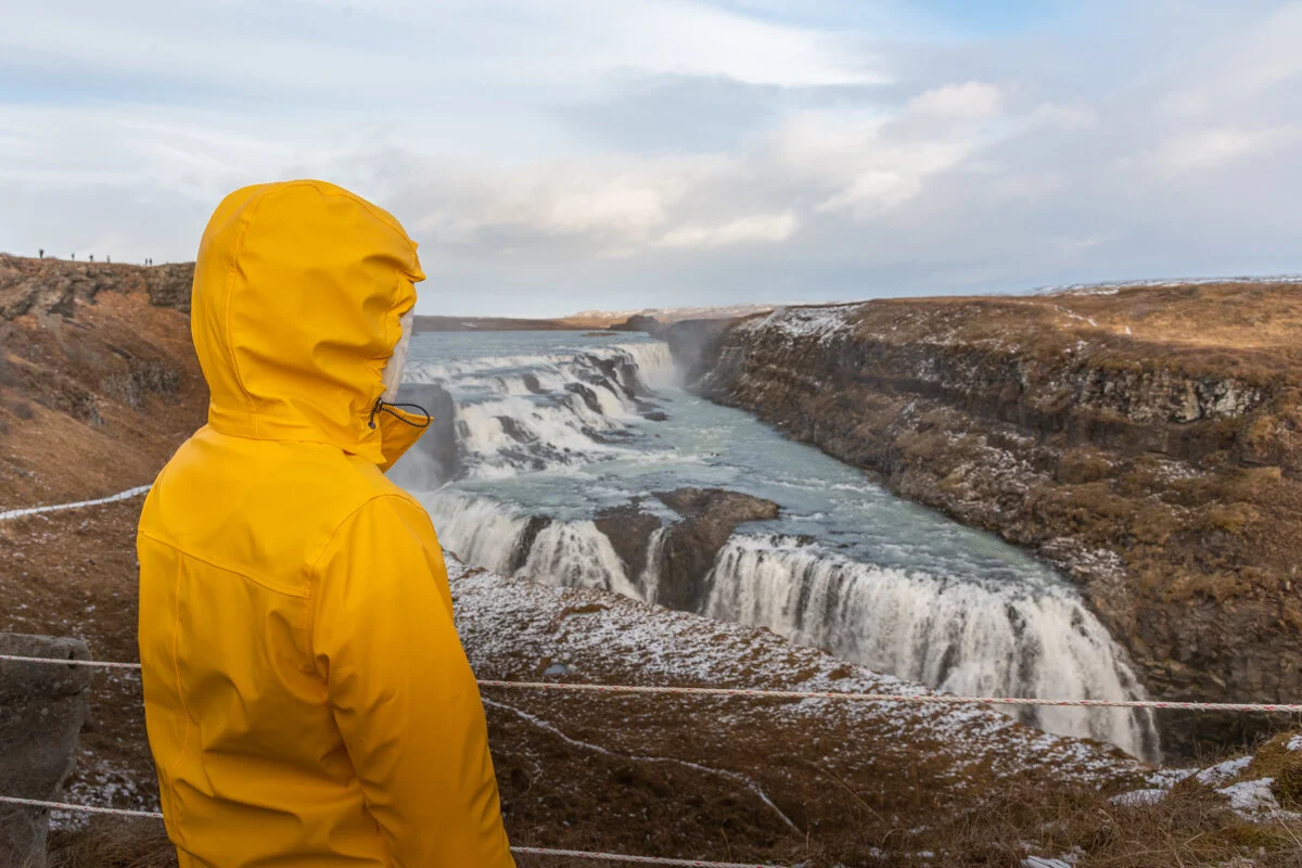 personne en veste jaune face à une cascade gelée