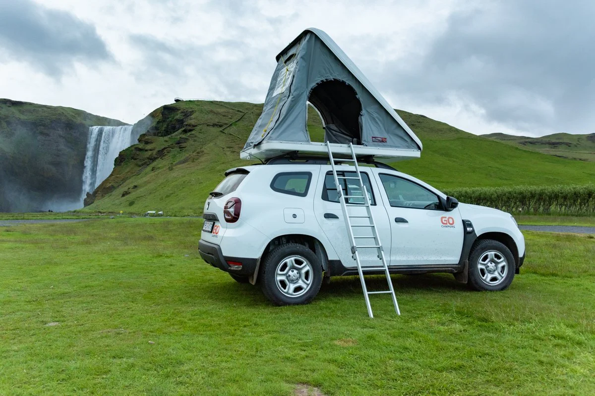 voiture avec tente de toit dans l'herbe avec Skogafoss en arrière plan